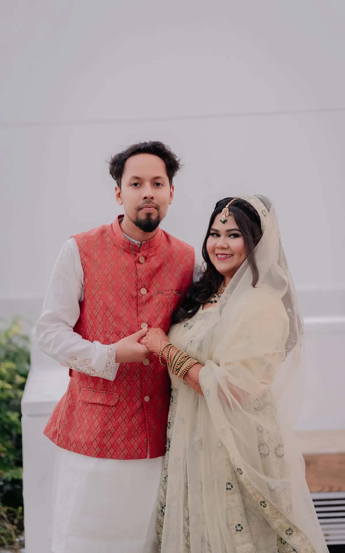 A bride in red and a groom in a turban standing together under the trees