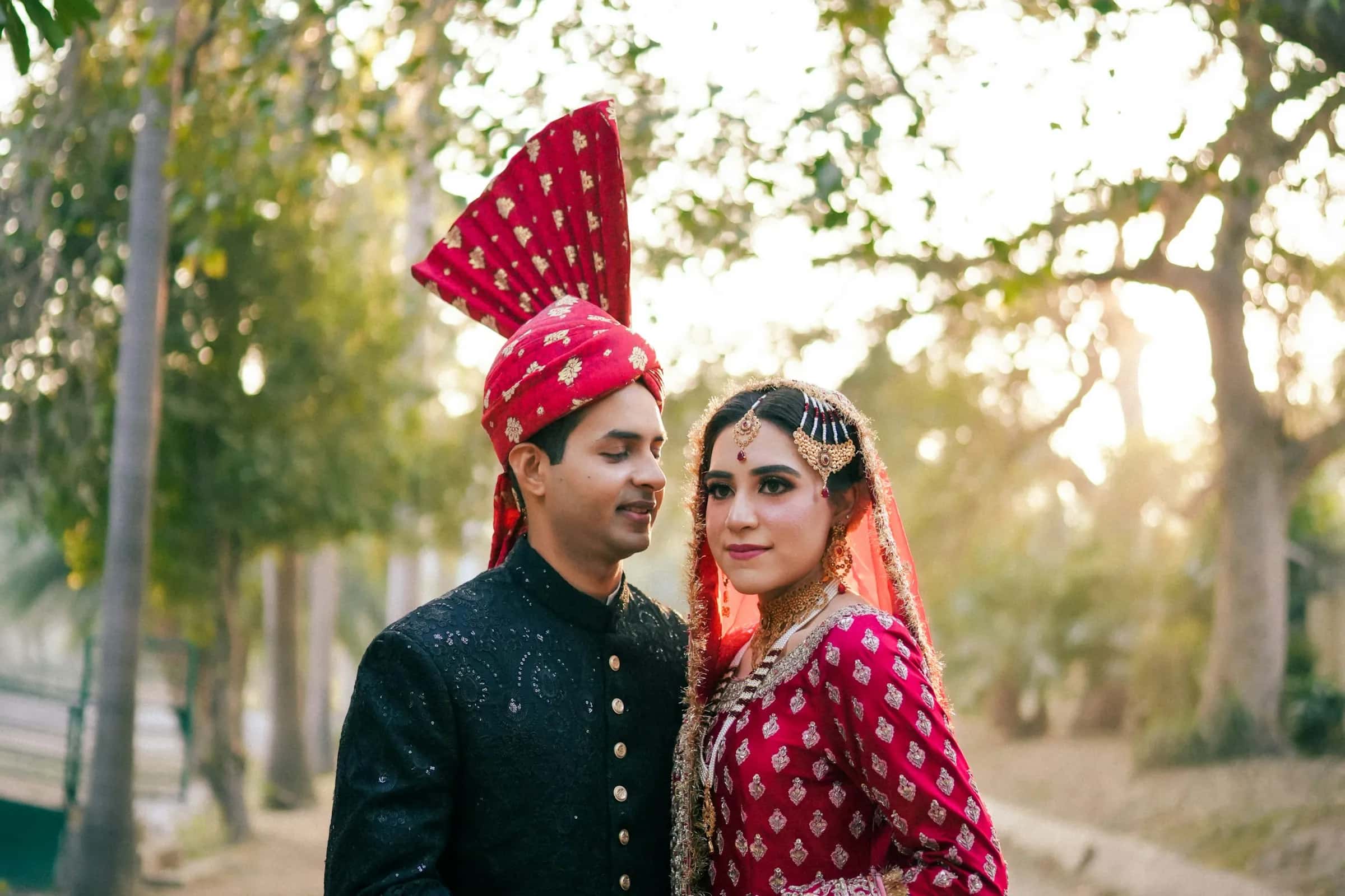 Ayesha & Bilal, A bride in a red lehenga and a groom in a cream sherwani on a candlelit stage