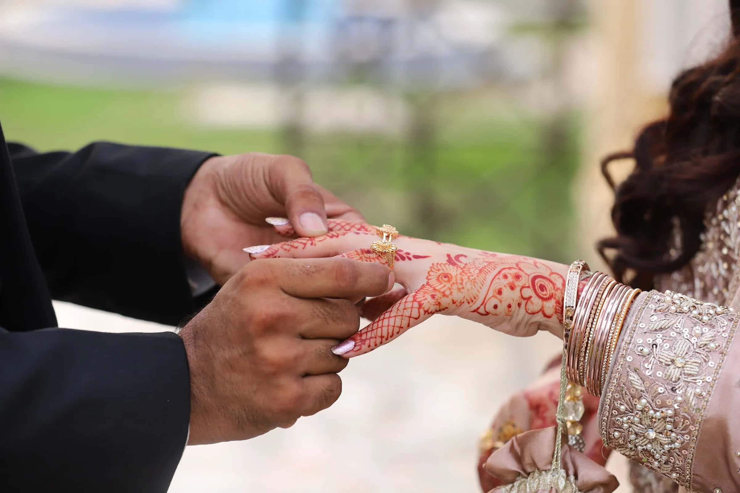A groom slipping a ring onto his bride's hennaed hand