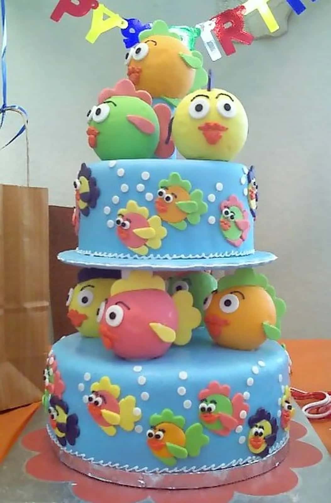 A two-tier first birthday cake covered in blue icing and little orange and green fish