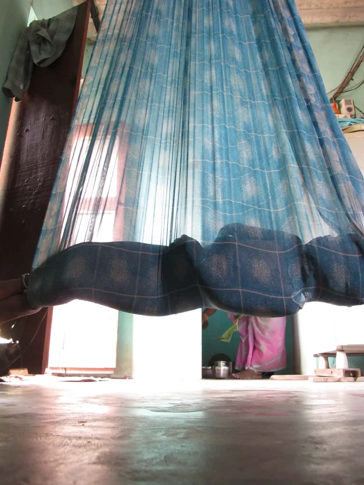 A cradle made from a blue sari hung from a beam, swaying above a cool stone floor