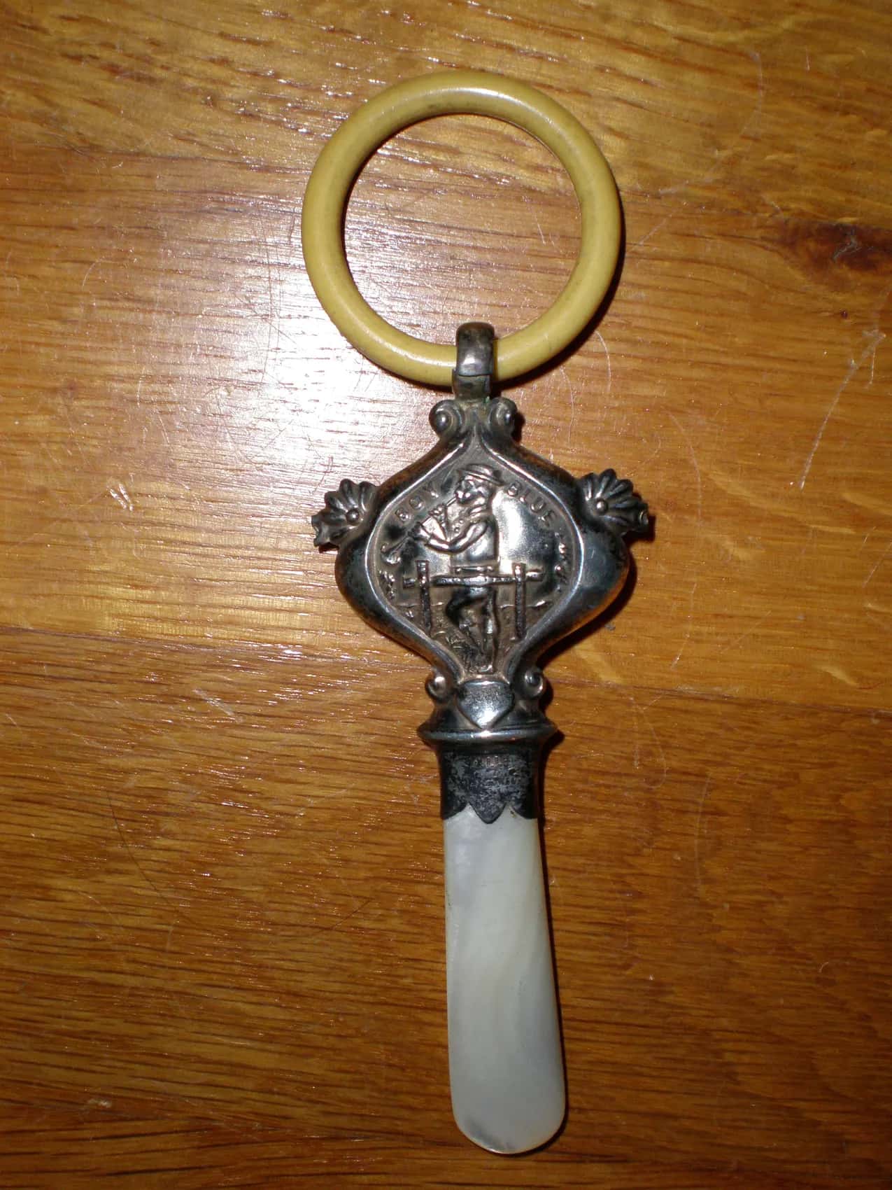 A silver baby rattle with a mother-of-pearl handle and a cream ring, on a wooden table