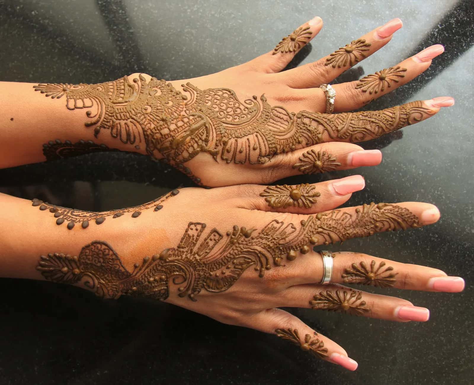 Two hands decorated with fine henna patterns, laid on a dark surface