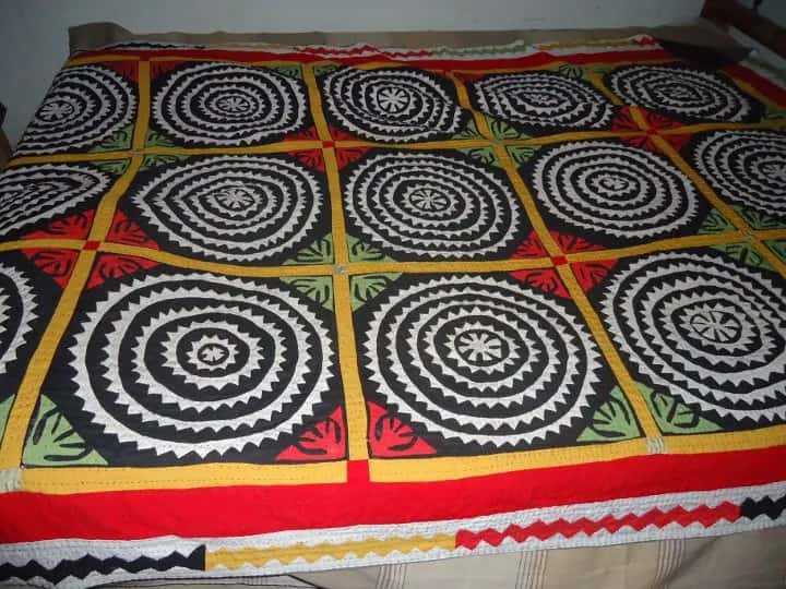 A Sindhi appliqué quilt on a bed, black and white circles on red and green
