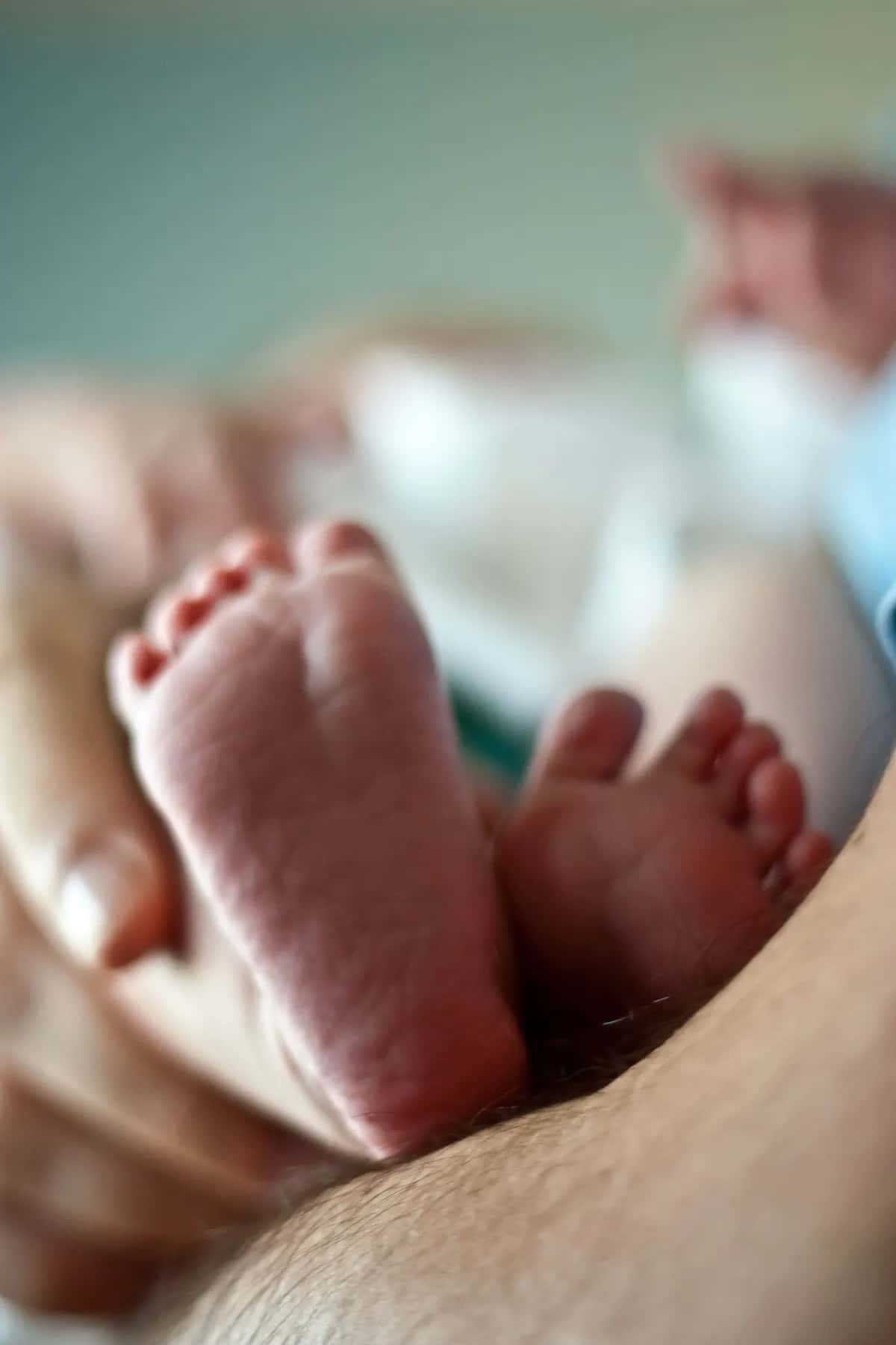 A newborn's feet held close against a father's skin, softly out of focus