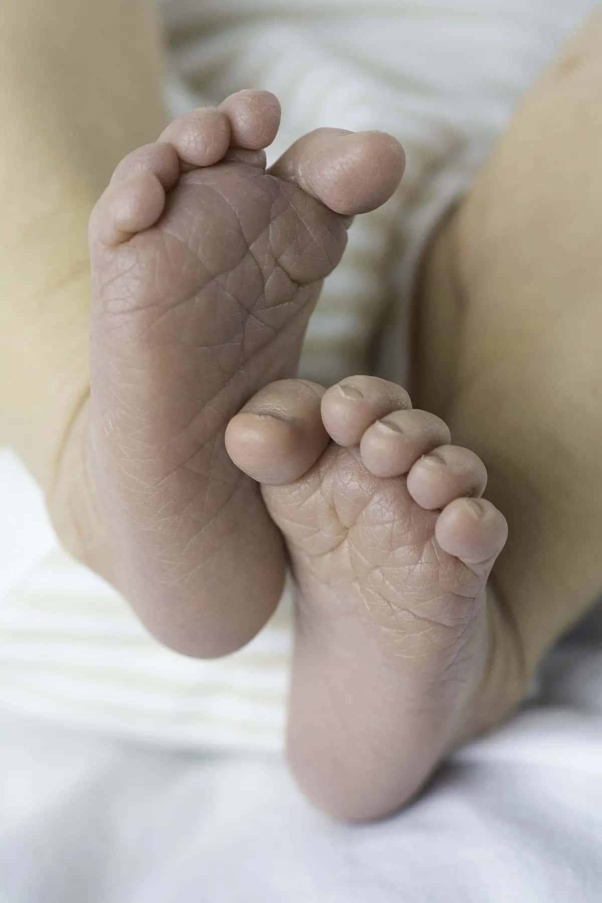 The soles of a newborn's two feet, creased and tiny, against a white blanket