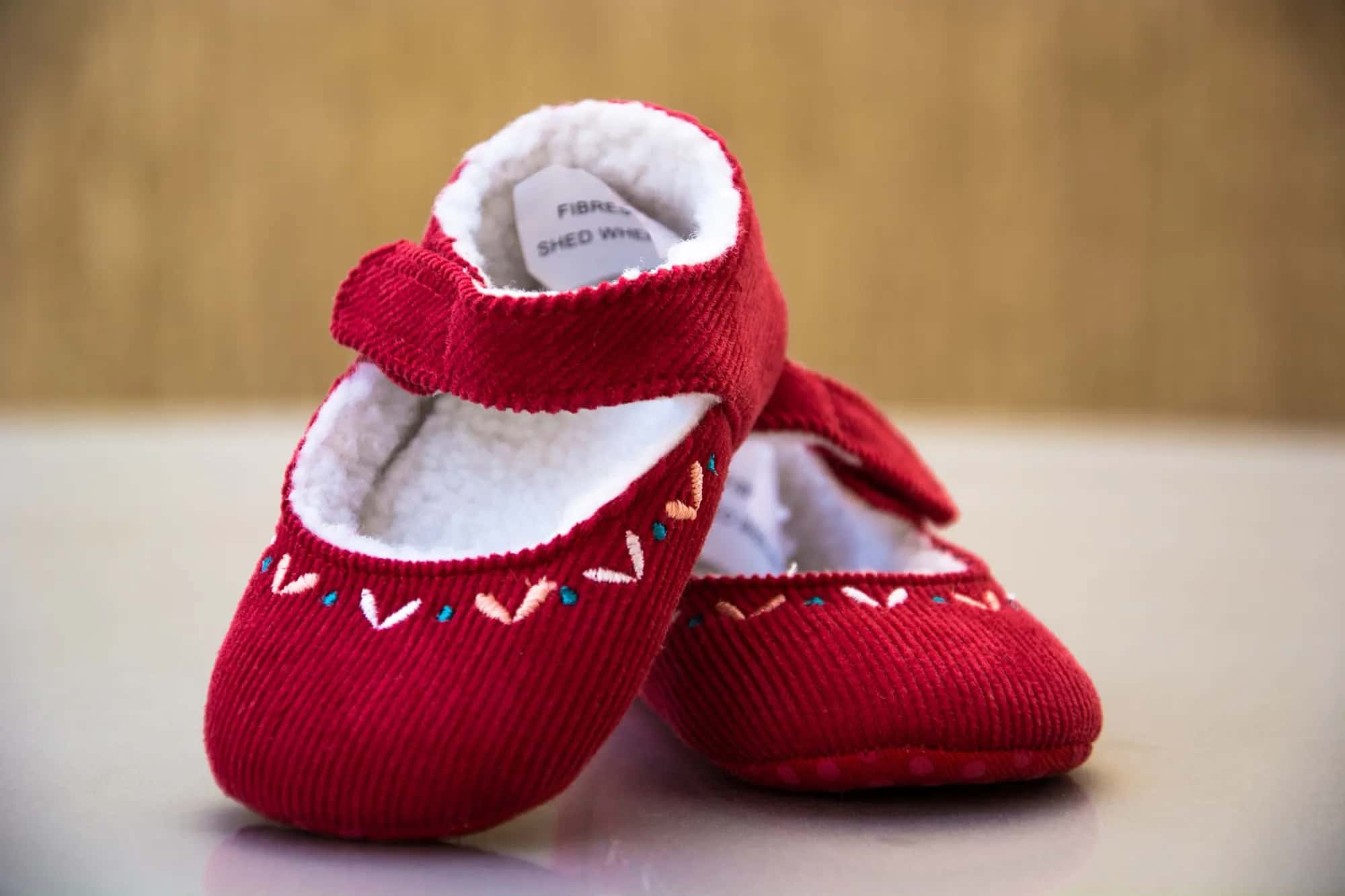 A pair of tiny red corduroy baby shoes with embroidered stitching