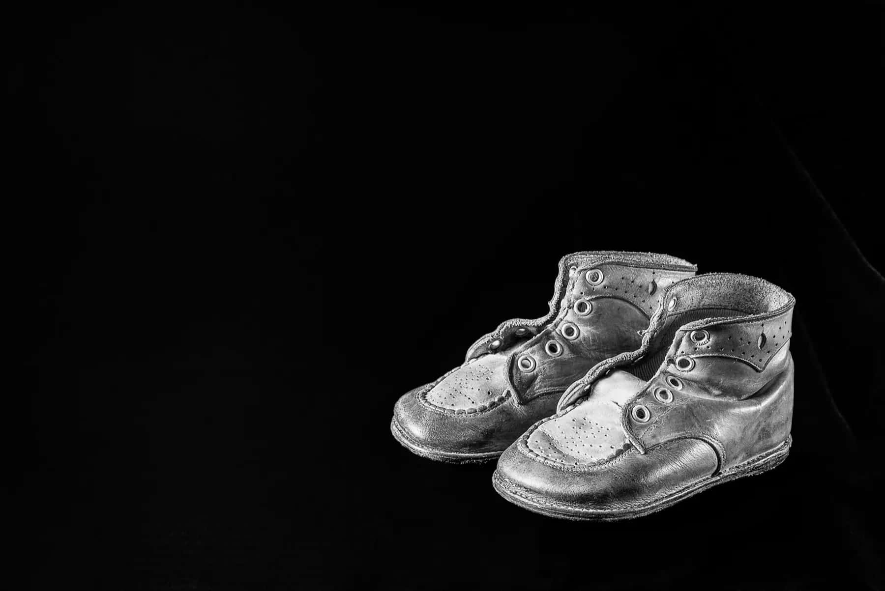 A pair of old leather baby shoes in black and white on a black background