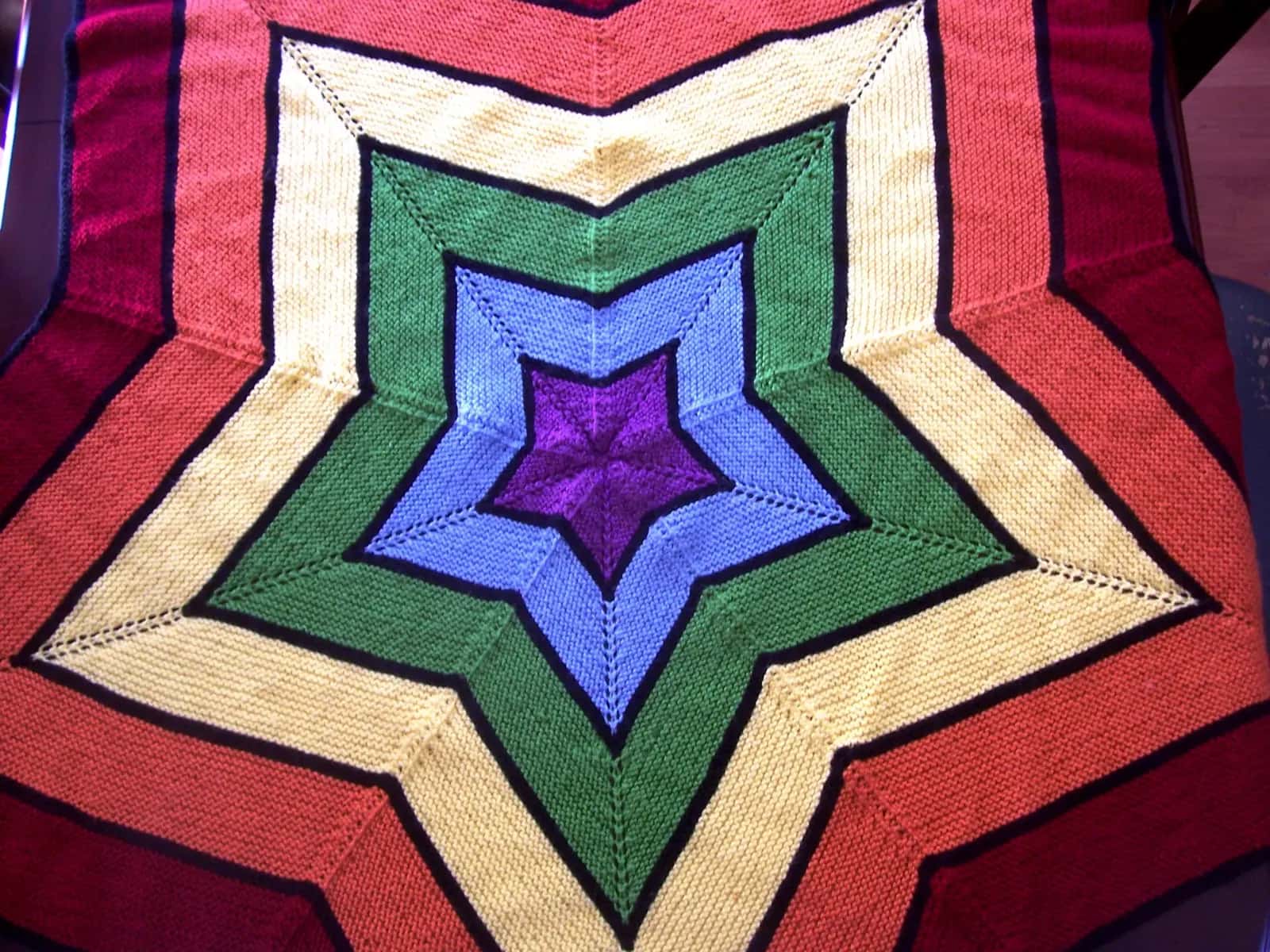 A knitted baby blanket worked as a five-pointed star in bands of colour