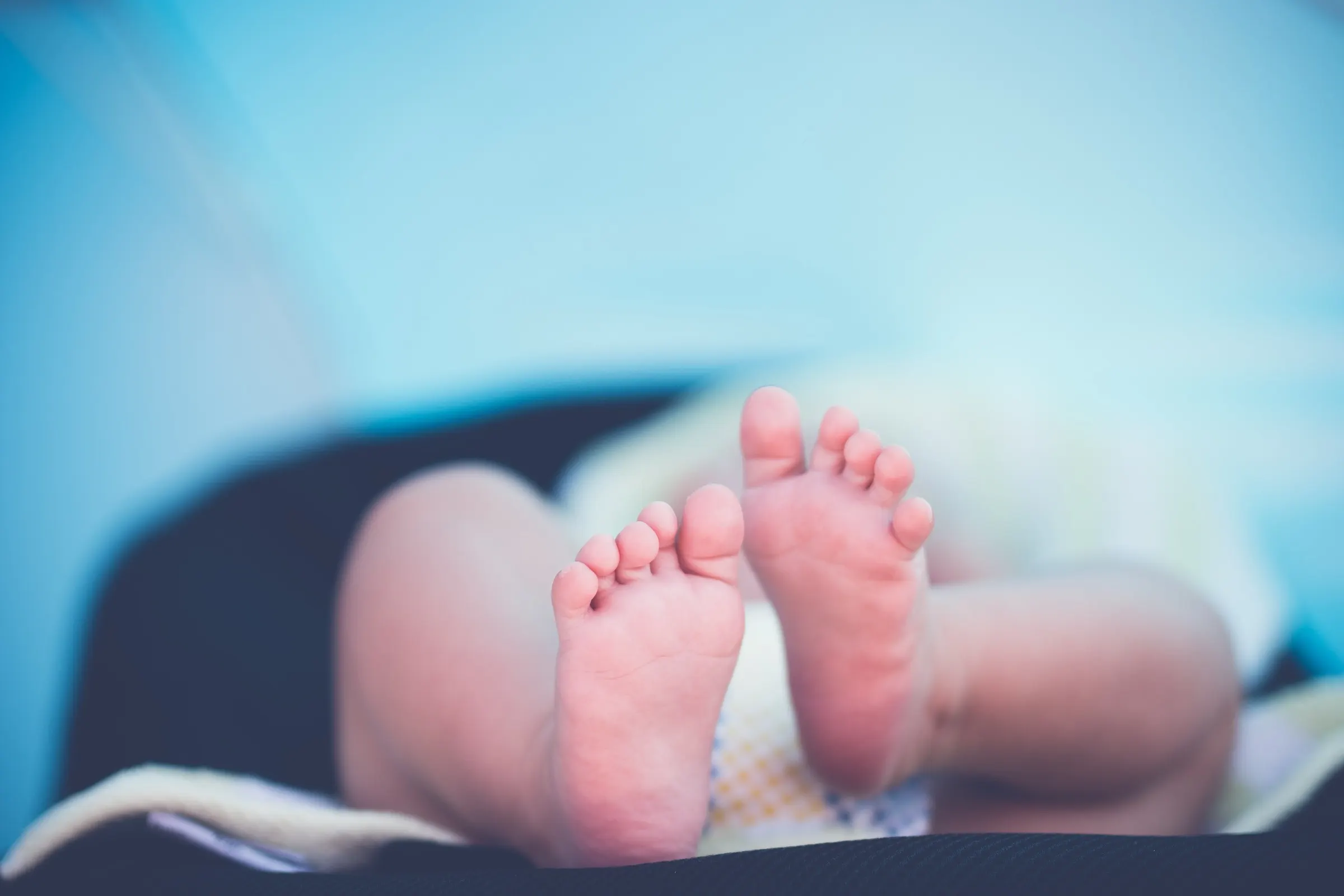 A newborn's two tiny feet, soles turned up, in soft blue light