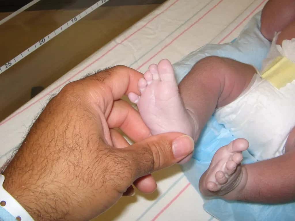 A newborn's foot held between a father's thumb and finger in a hospital cot
