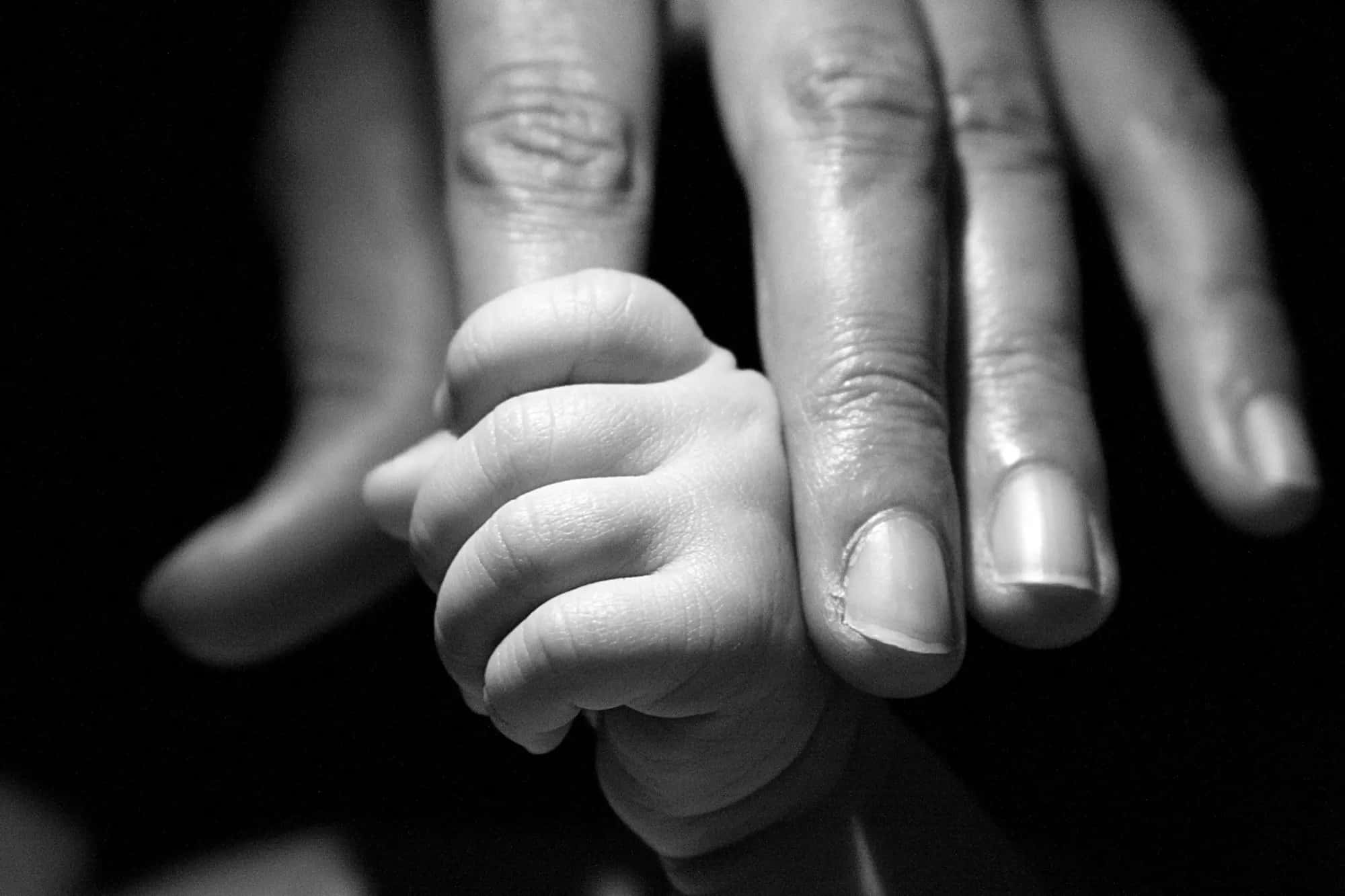 A tiny hand gripping a grown-up's finger, in black and white