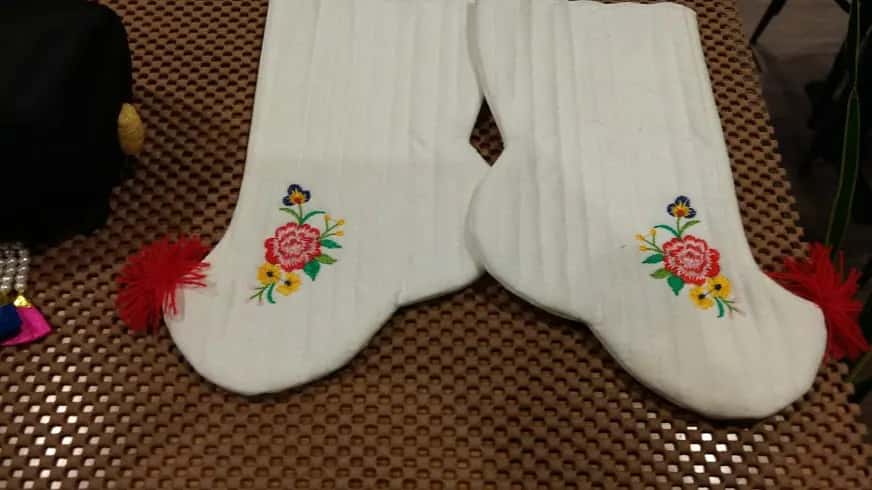 Two white baby socks embroidered with flowers and tied with red tassels