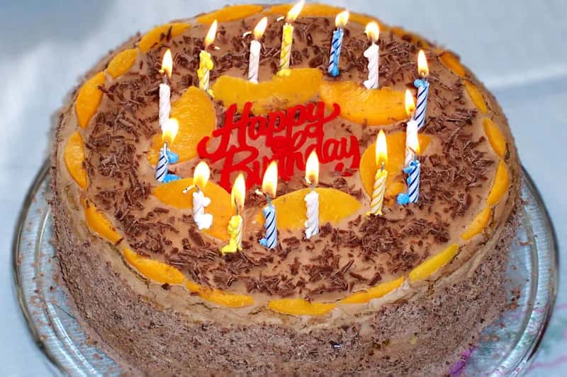 A round cake with orange slices, grated chocolate and lit candles