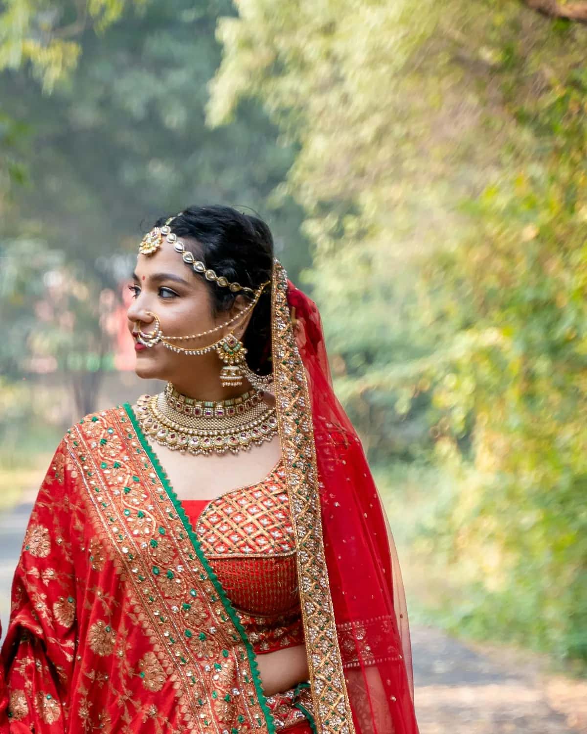 The bride in a red and gold lehenga, walking down a leafy path