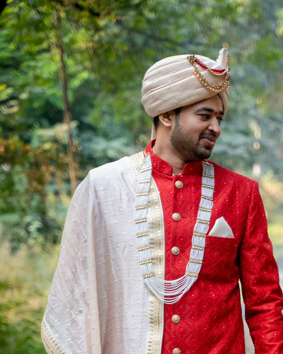 The groom in a red sherwani, walking beside her