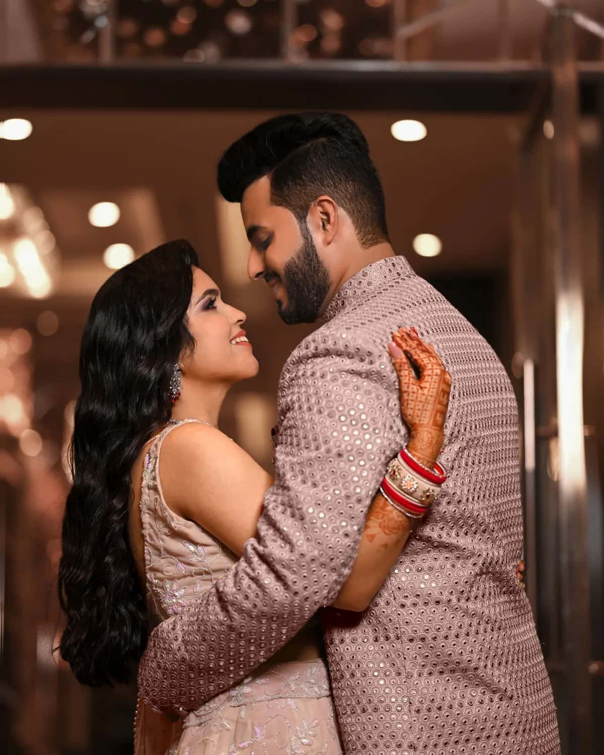 The couple laughing in matching blush outfits under fairy lights