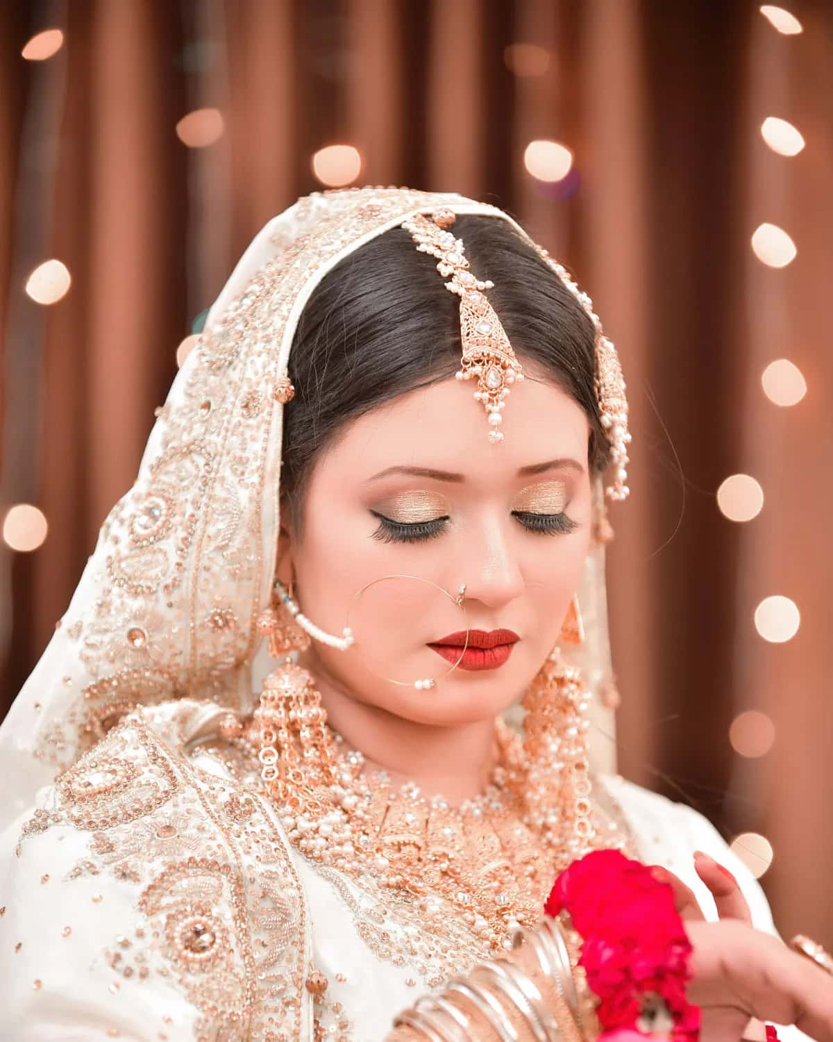 A bride in ivory and gold holding red flowers