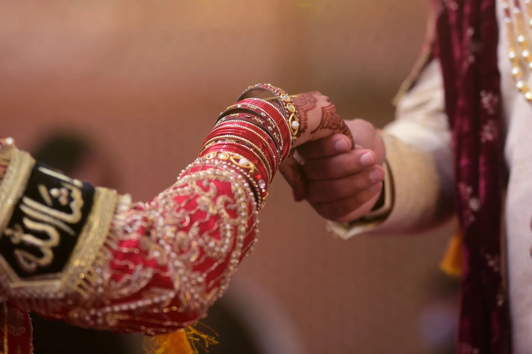 Hands held at the nikah, embroidered sleeve and red bangles