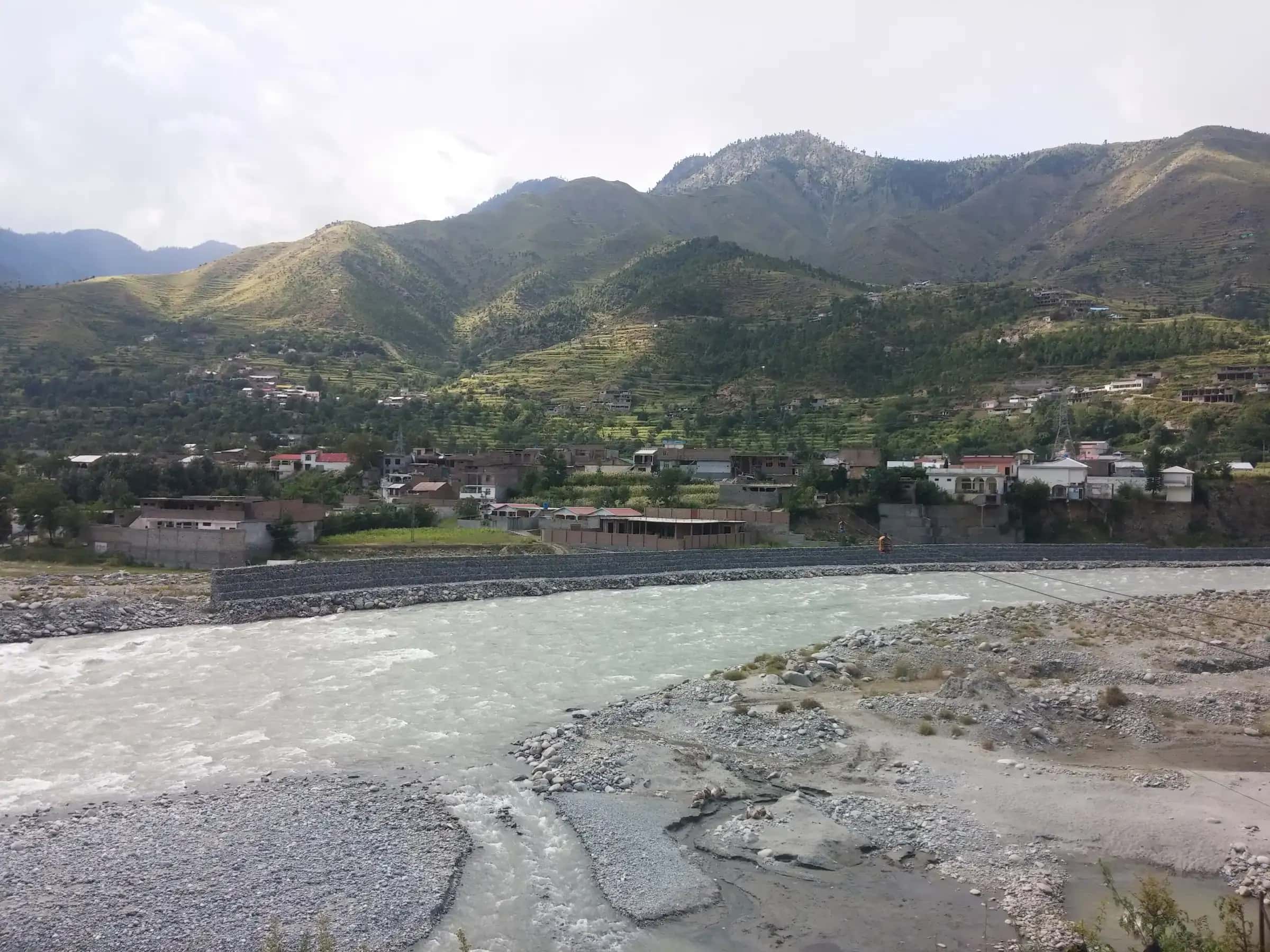 The Swat river running wide and clear past Kalam, green hills and snow peaks beyond