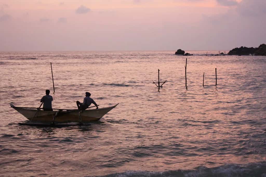 Two fishermen in a small boat on a pink sea at dawn off Mirissa