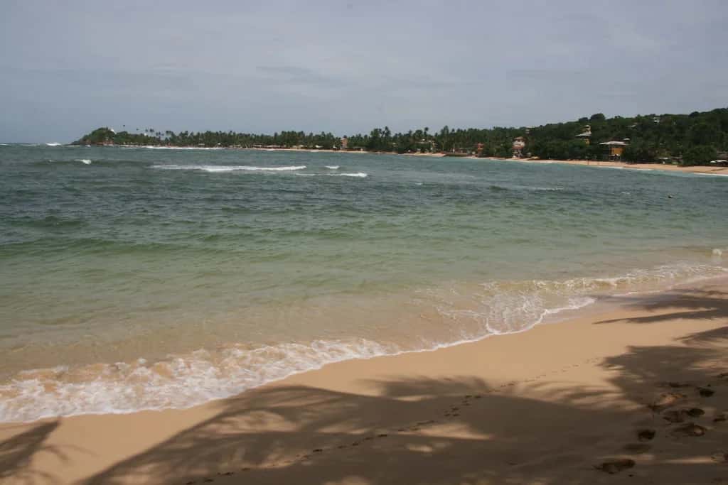 Green water and pale sand along the curve of Unawatuna bay