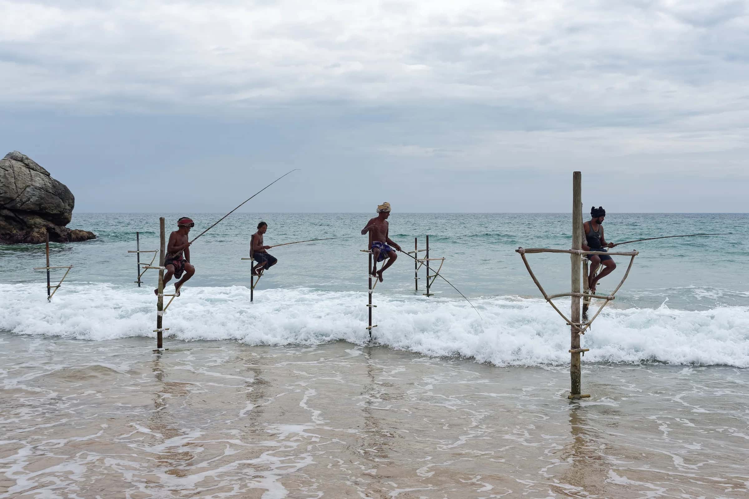 Four stilt fishermen perched on their poles in the surf near Ahangama