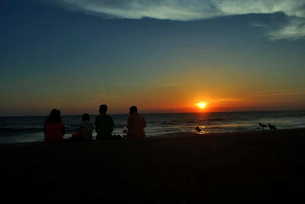 People sitting on the sea wall at Galle Face Green as the sun sets into the sea