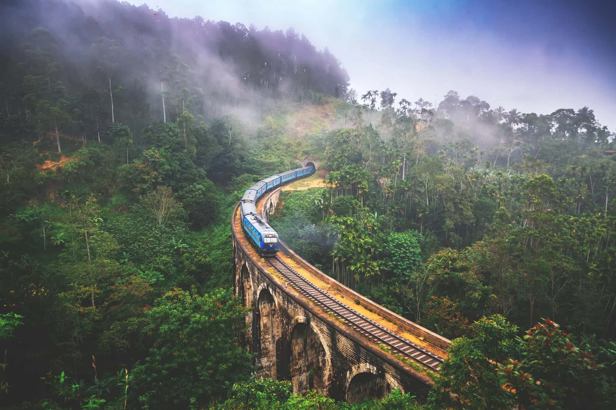The blue train crossing the Nine Arch Bridge at Ella through mist and tea