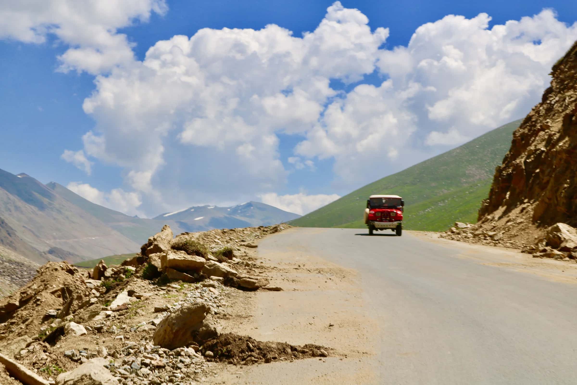 A red jeep coming up the mountain road in the Naran valley under summer clouds