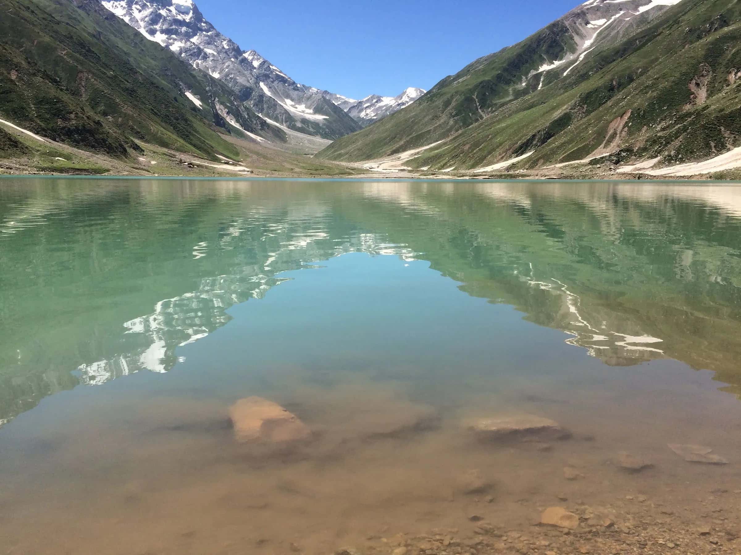 Saiful Muluk lake, still and green under snow-streaked slopes