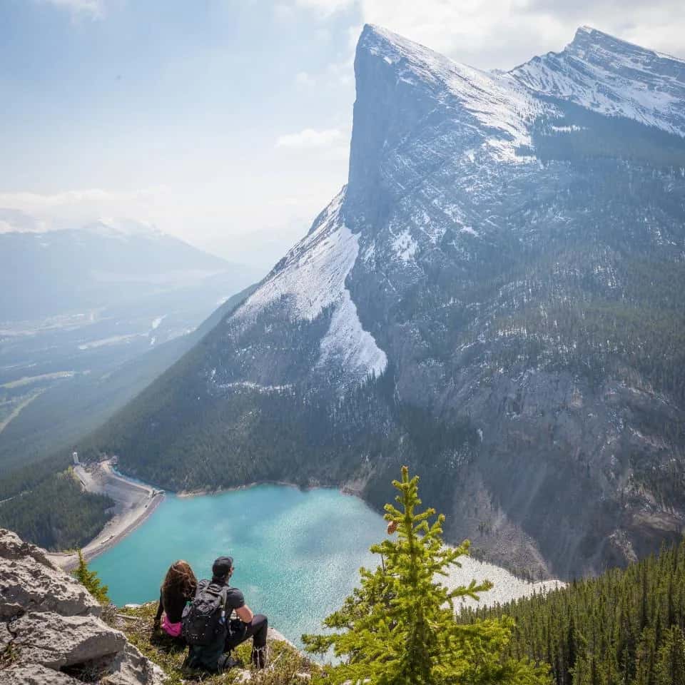 A couple seen from behind, sitting on a rocky ledge above a turquoise lake