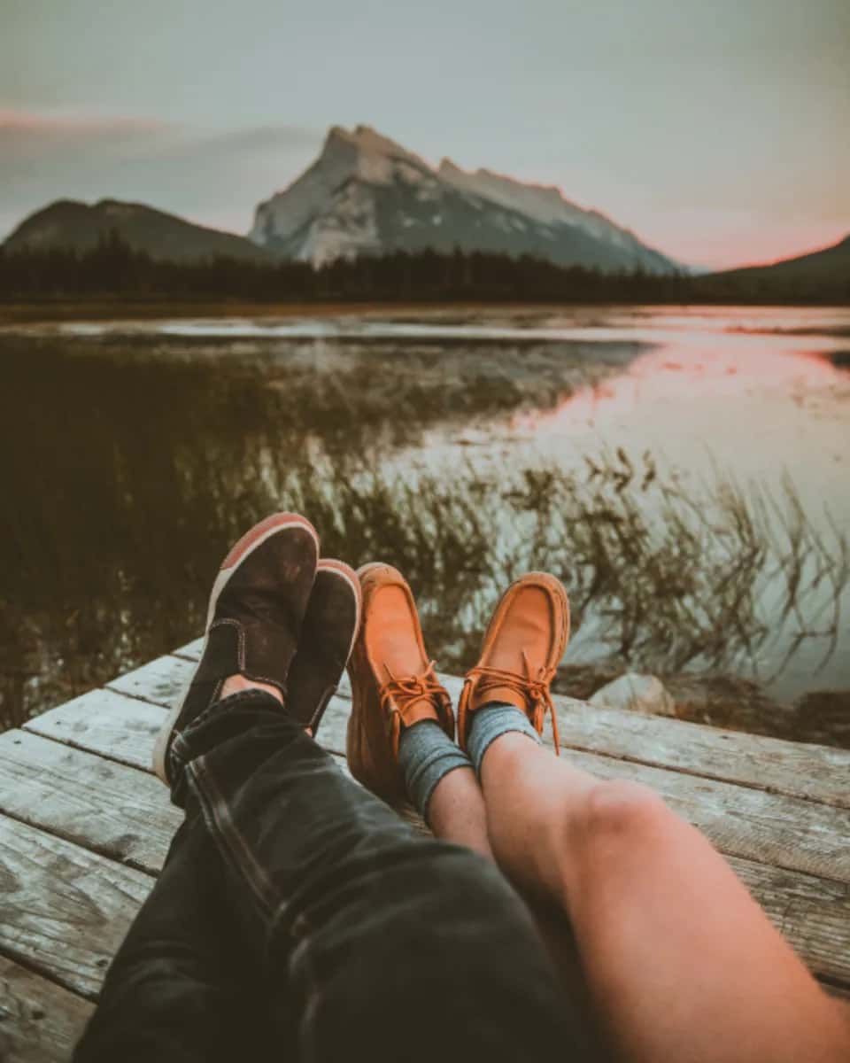 Two pairs of feet up on a wooden jetty, a lake and a mountain beyond