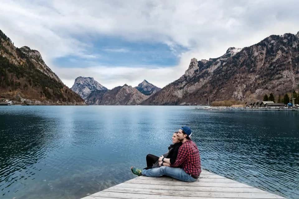 A couple sitting close on a jetty at a mountain lake
