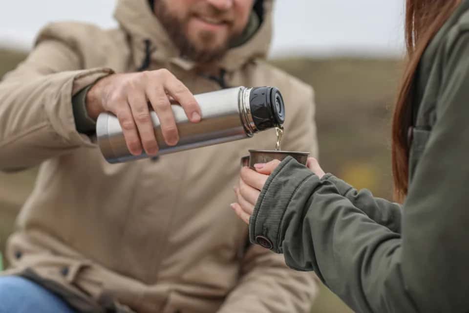 Chai poured from a steel thermos into a cup held out by a gloved hand