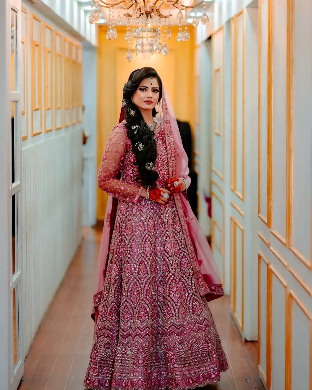 A bride in a jewelled lehenga in a long bright corridor