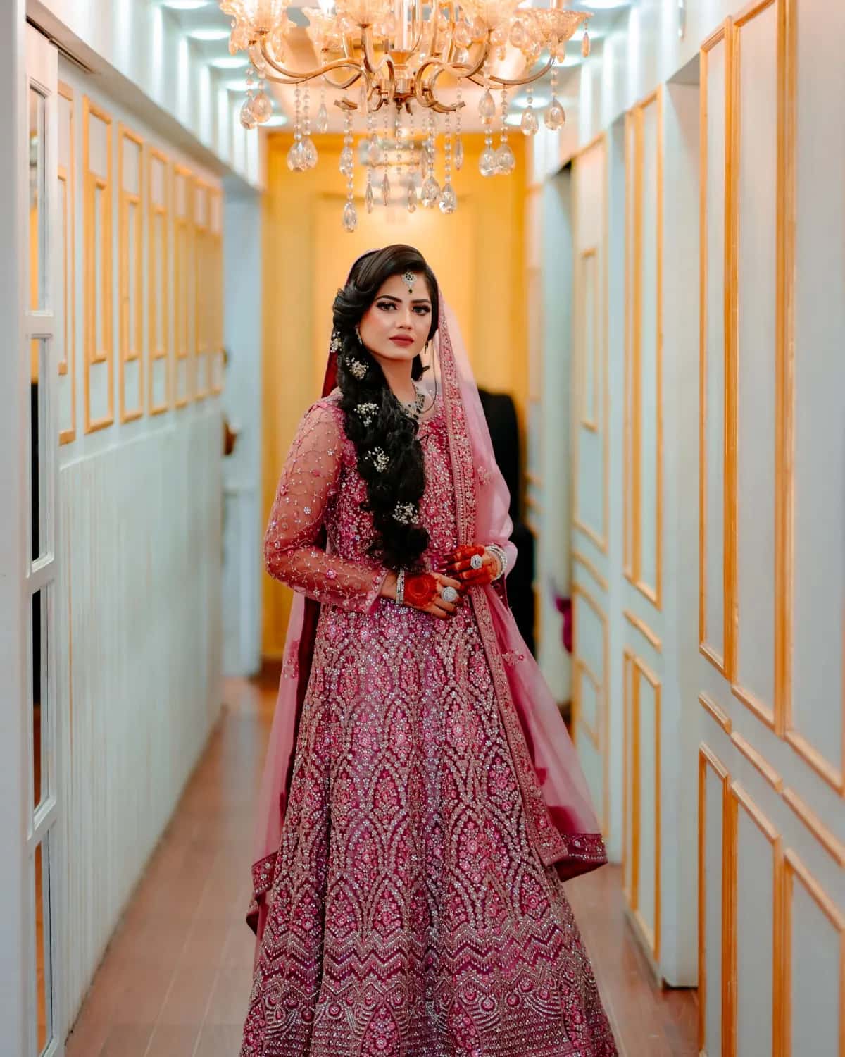 A bride in a pink lehenga under a crystal chandelier