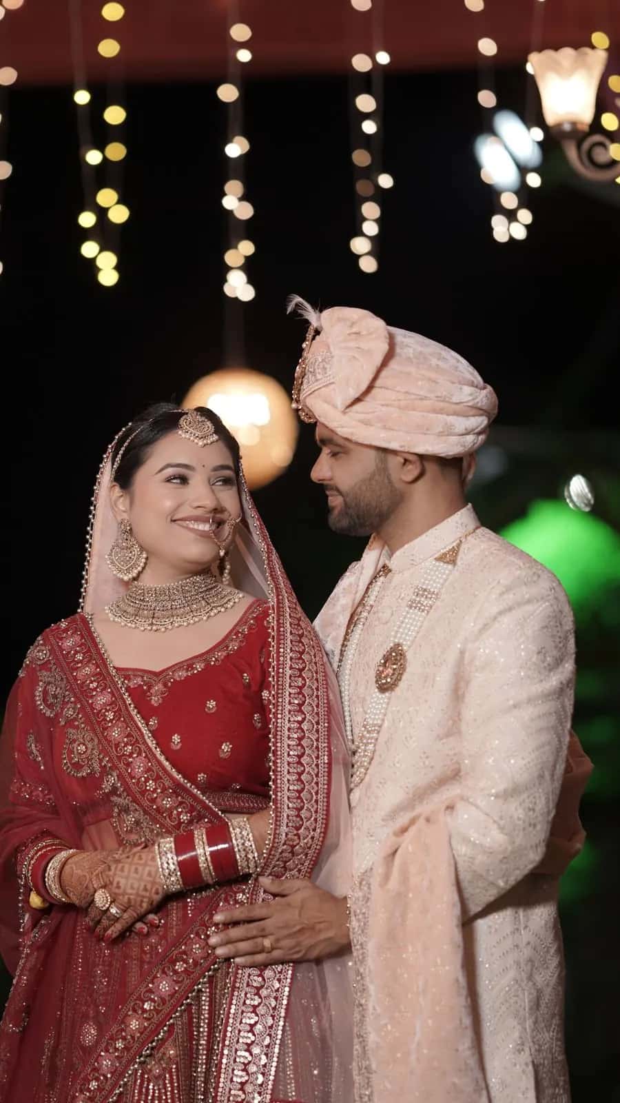 The bride and groom smiling at each other between pink drapes and fairy lights