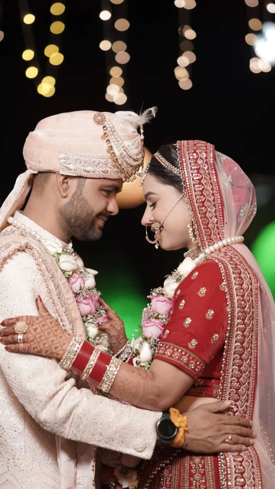 A bride and groom holding each other under fairy lights and deep red drapes