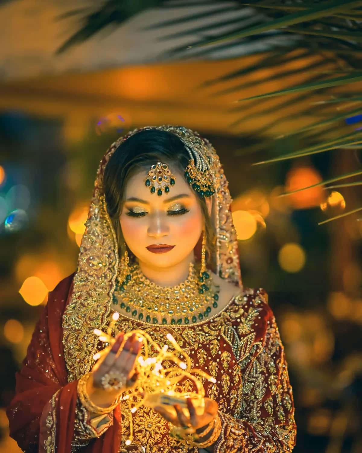 The bride in red and gold holding a string of fairy lights