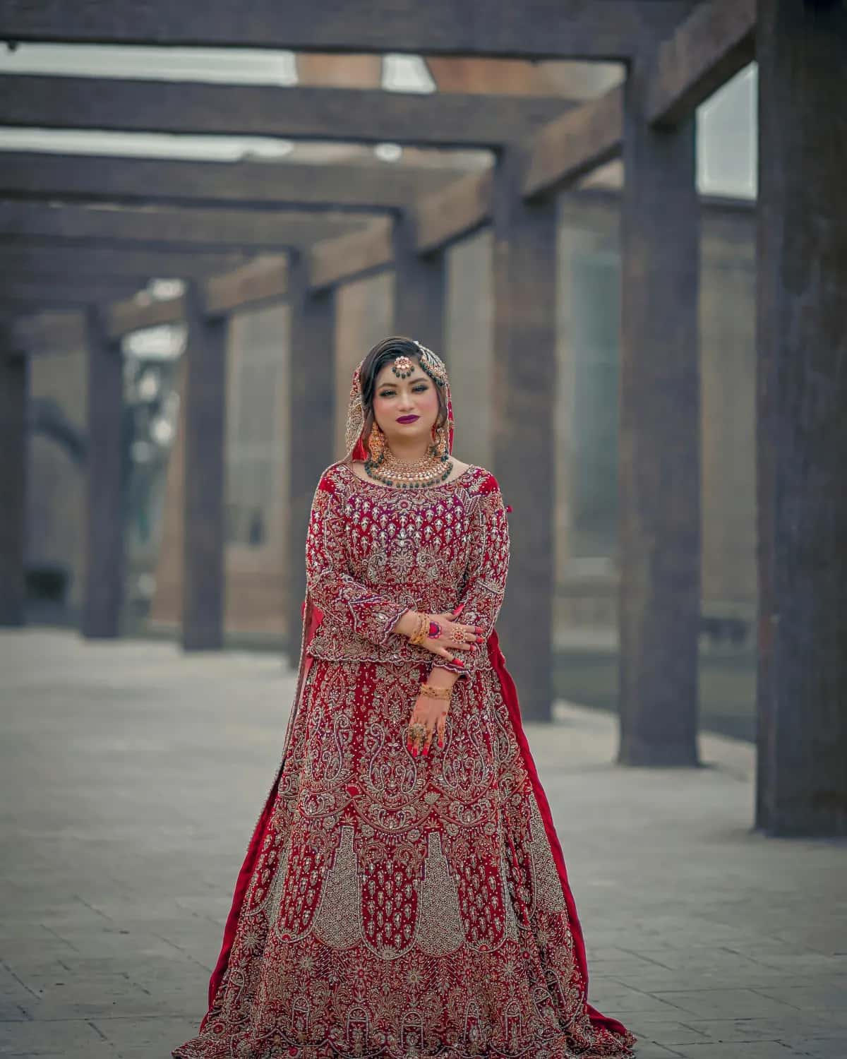 A bride in a red lehenga under a wooden pergola
