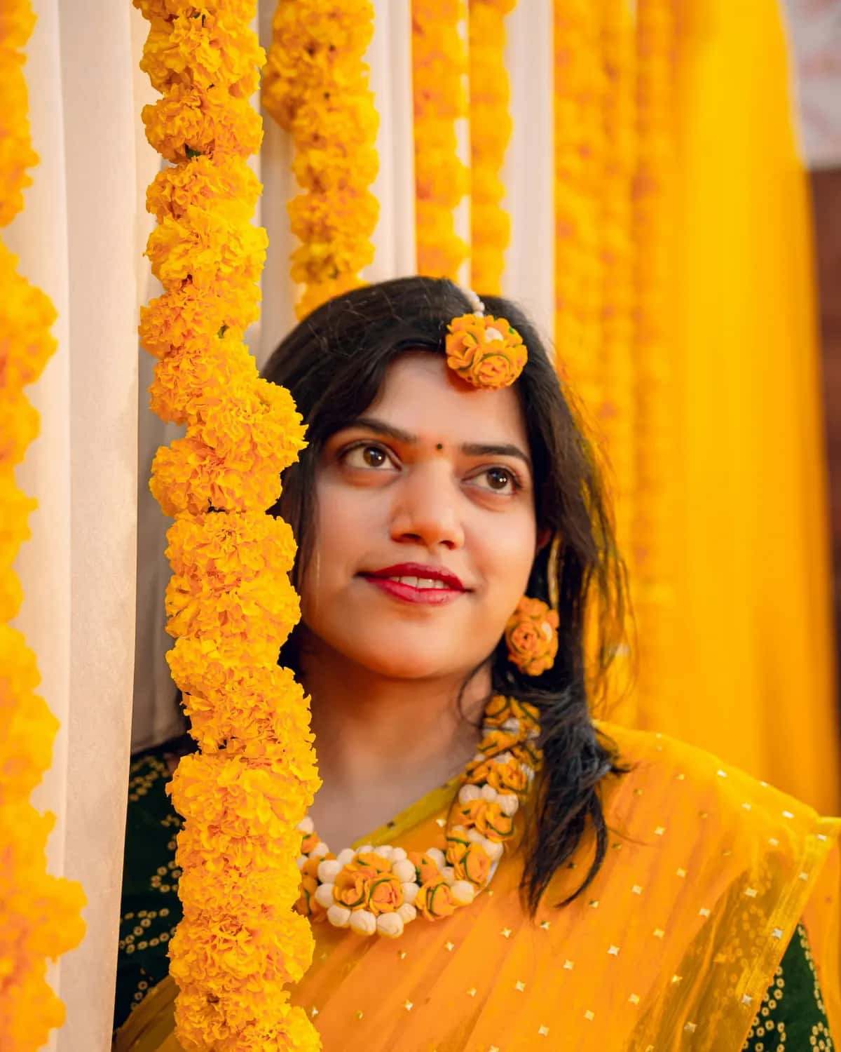 A girl in yellow peeking out from behind marigold garlands