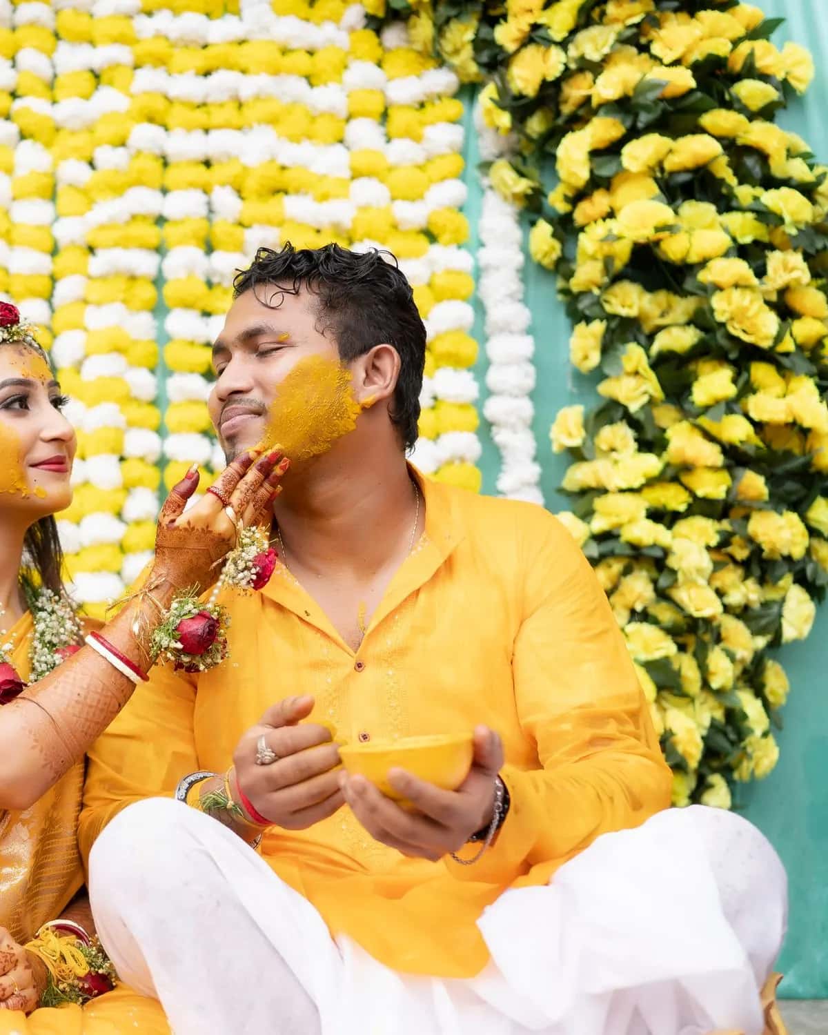 The groom with turmeric on his face holding a bowl of haldi