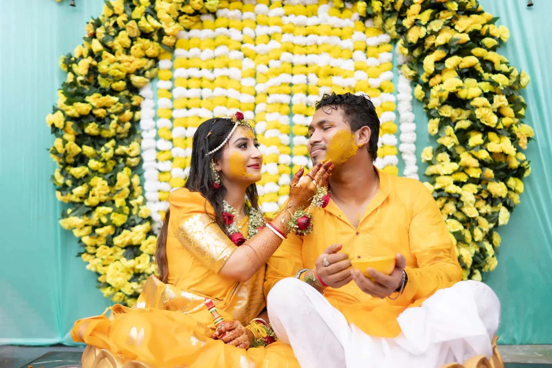 The bride feeding the groom sweets in front of a marigold wall