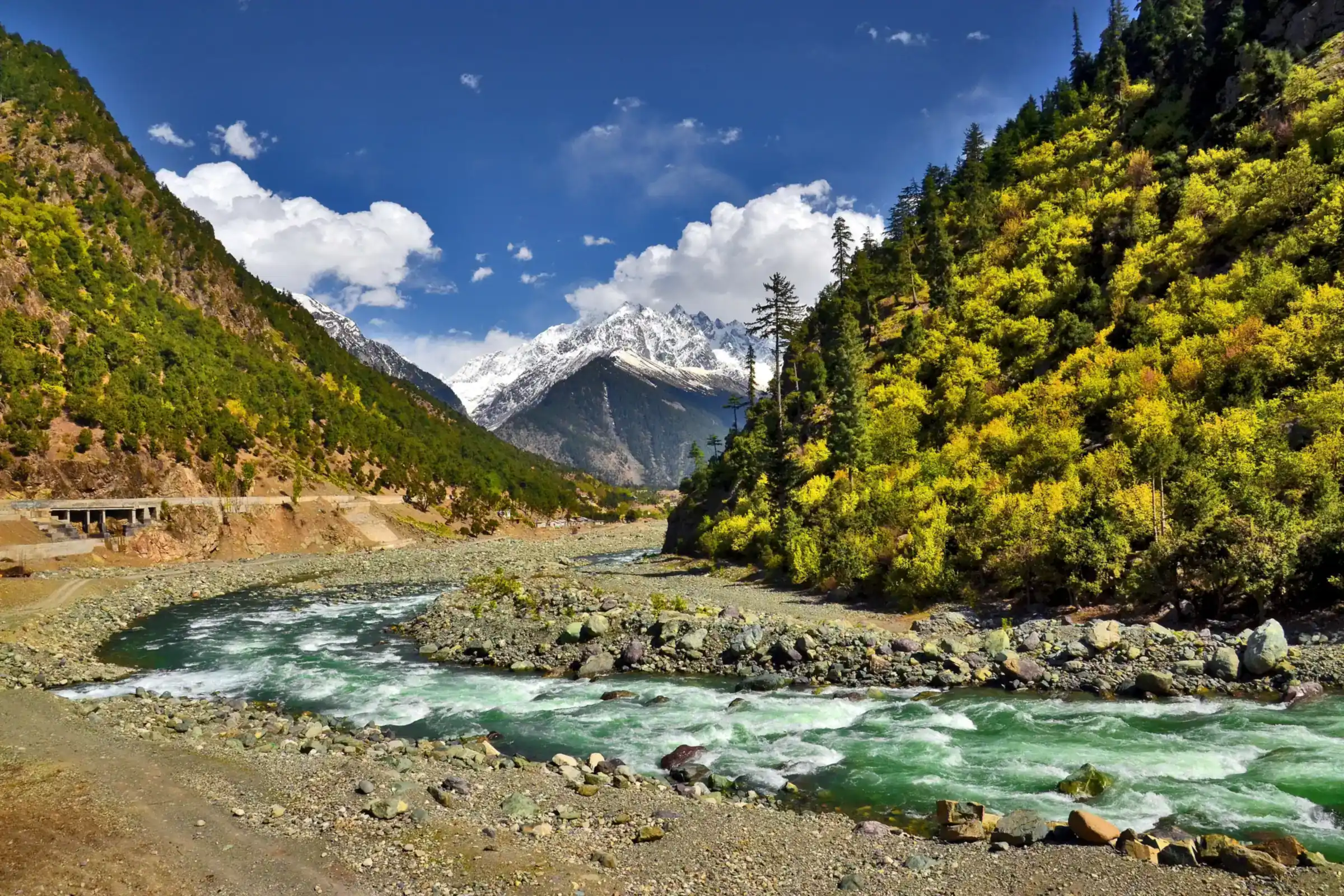 The Swat river rushing green over stones at Kalam, a snow peak and spring forest beyond